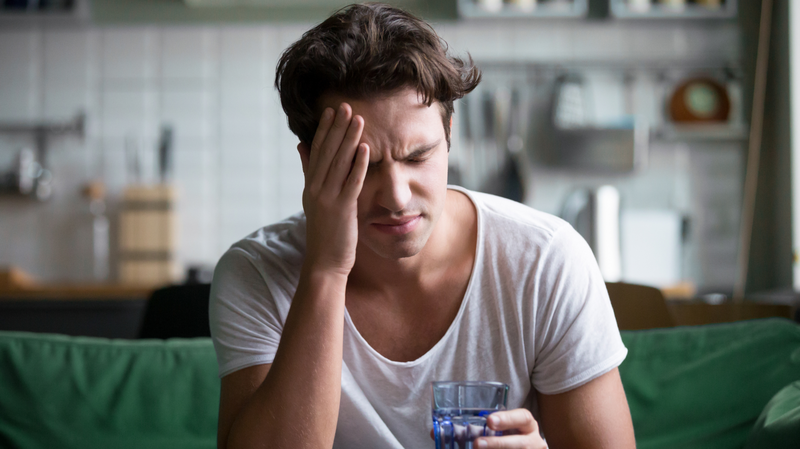 man with migraine holding head and glass of water