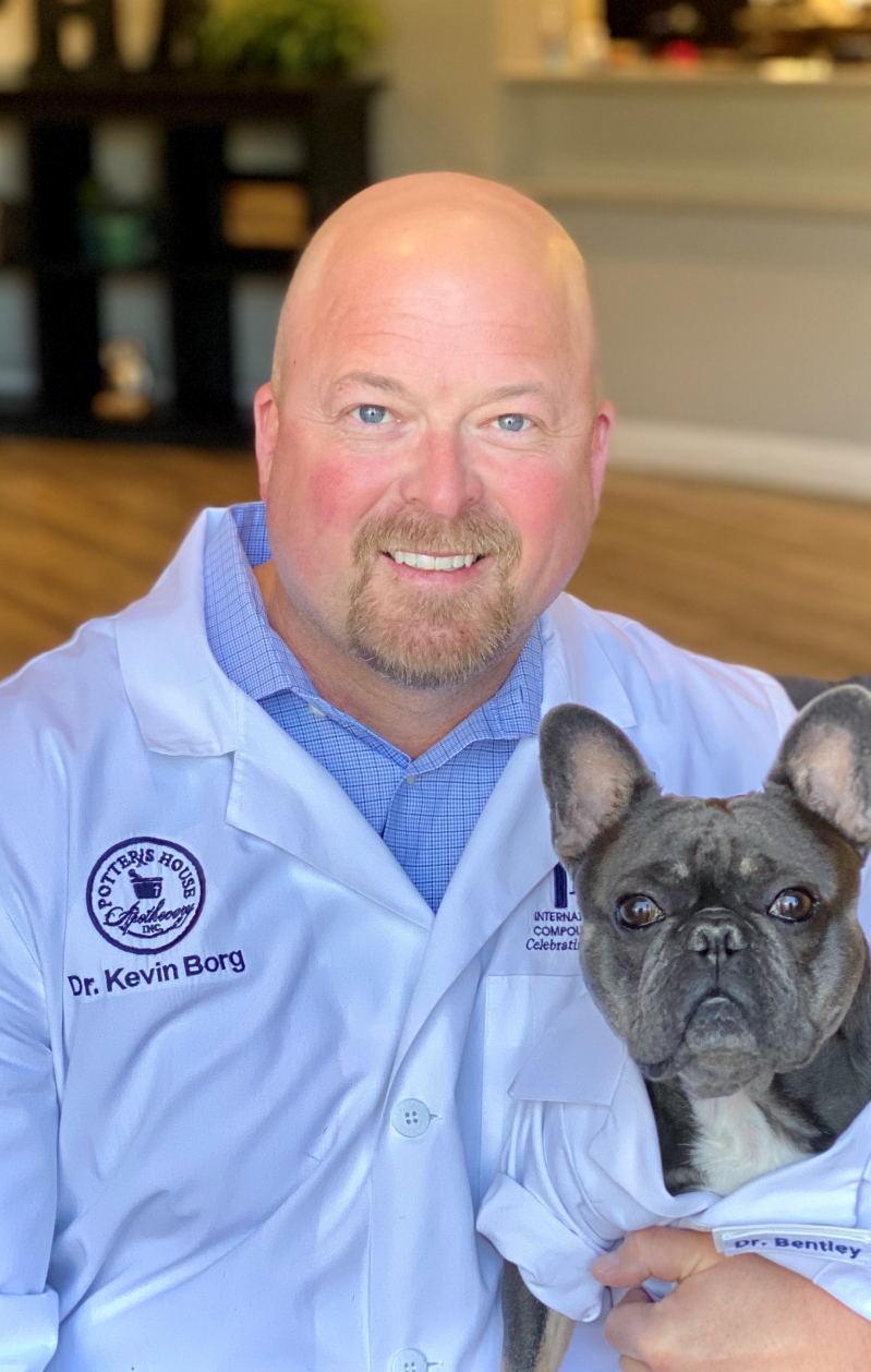 Dr. Kevin Borg holding dog in lab coat that says Dr. Bentley